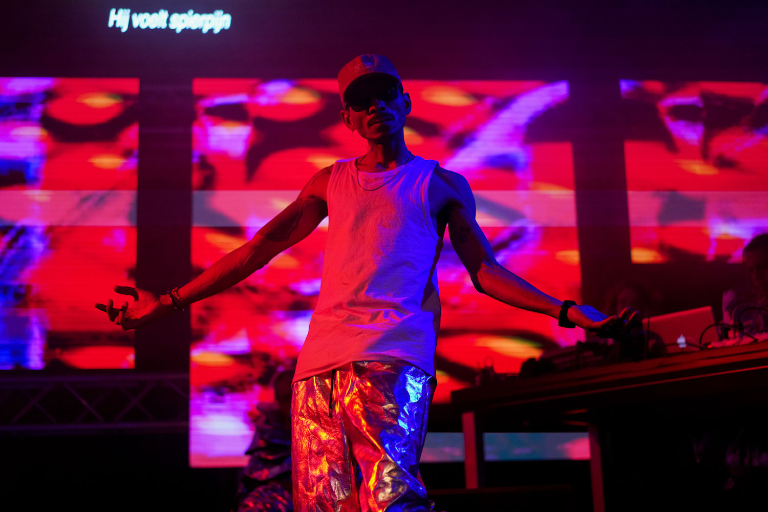 A person dances in a club setting with projections behind and red-purple light