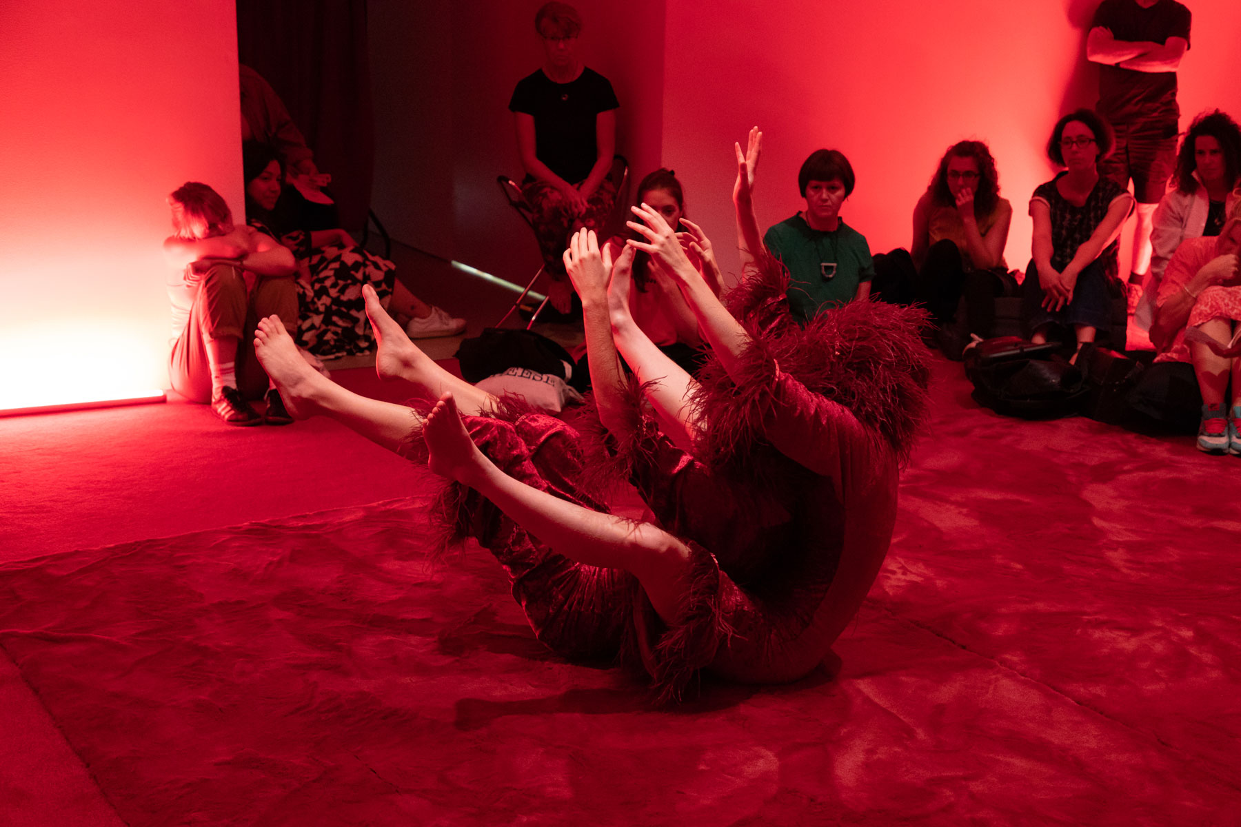 A dancer raises their limbs, wearing a red costume in a red installation