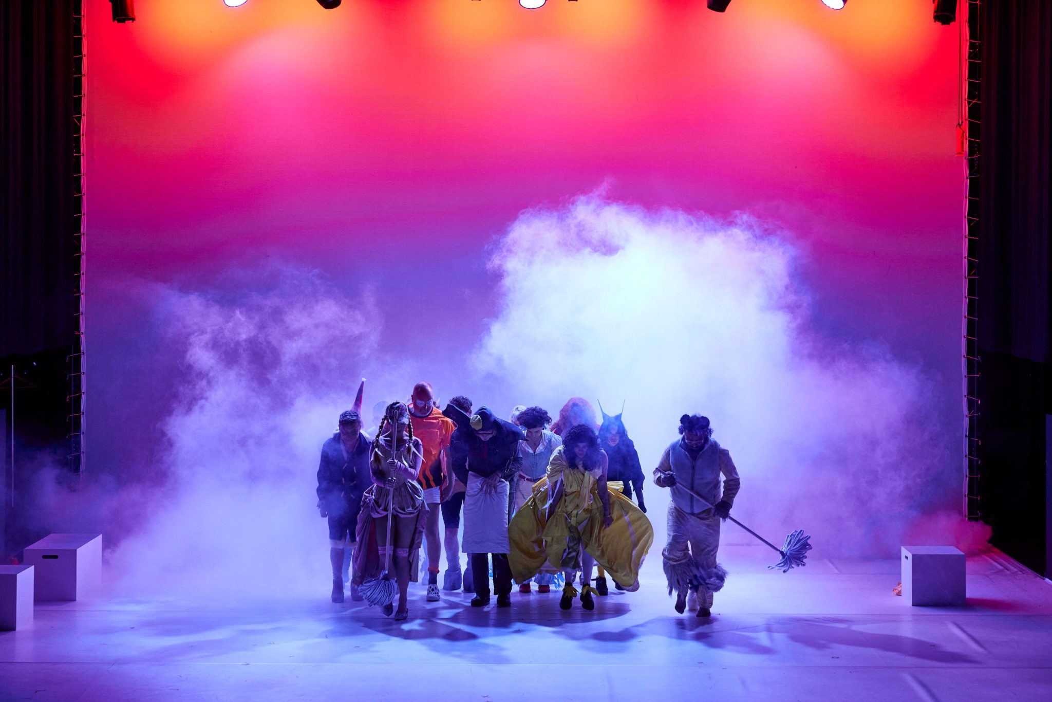 A cast of characters in fairytale costumes with orange light behind