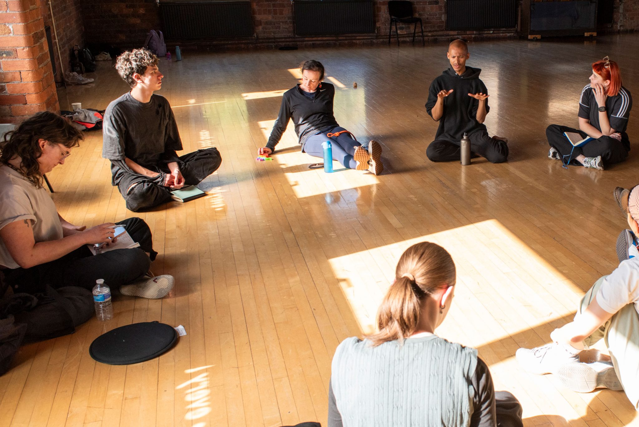 People gather in conversation sat in a circle in a dance studio